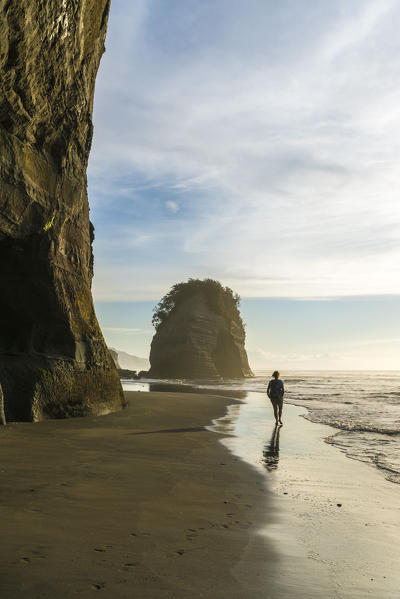 Woman walking on the beach towards Elephant Rock. Tongaporutu, New Plymouth district. Taranaki region, North Island, New Zealand. (MR)