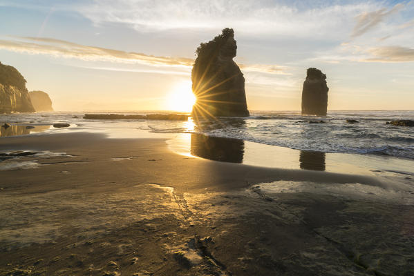 The sun in setting down behind the Three Sisters. Tongaporutu, New Plymouth district. Taranaki region, North Island, New Zealand.