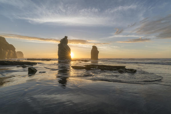 The sun in setting down behind the Three Sisters. Tongaporutu, New Plymouth district. Taranaki region, North Island, New Zealand.