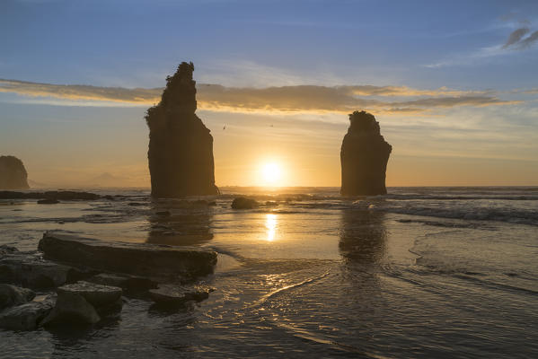 The sun in setting down behind the Three Sisters. Tongaporutu, New Plymouth district. Taranaki region, North Island, New Zealand.