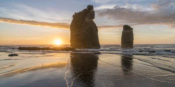 The sun in setting down behind the Three Sisters. Tongaporutu, New Plymouth district. Taranaki region, North Island, New Zealand.