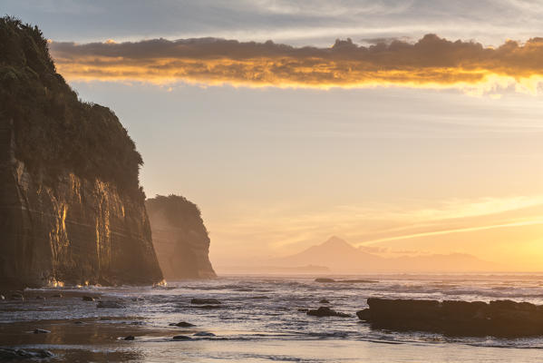 Elephant rock and Mount Taranaki silhouette in the background, at sunset. Tongaporutu, New Plymouth district. Taranaki region, North Island, New Zealand.