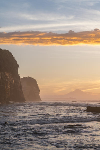 Elephant rock and Mount Taranaki silhouette in the background, at sunset. Tongaporutu, New Plymouth district. Taranaki region, North Island, New Zealand.