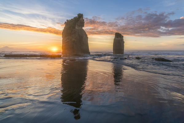 The sun in setting down behind the Three Sisters. Tongaporutu, New Plymouth district. Taranaki region, North Island, New Zealand.