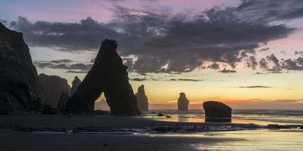 Sunset at the Three Sisters beach, with Mt Taranaki seen through the rock cave.  Tongaporutu, New Plymouth district. Taranaki region, North Island, New Zealand.