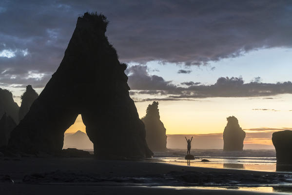 Woman's silhouette at the Three Sisters beach, with Mt Taranaki seen through the rock cave.  Tongaporutu, New Plymouth district. Taranaki region, North Island, New Zealand.