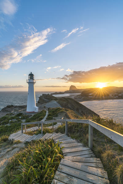 The sun is setting down behind Castle Rock and Castlepoint lighthouse.  Castlepoint, Wairarapa region, North Island, New Zealand.