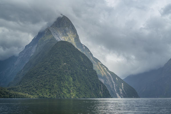Boat  and Mitre Peak under a moody sky in Milford Sound. Fiordland NP, Southland district, Southland region, South Island, New Zealand.