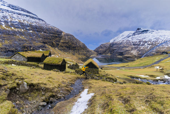 Hiker jumping on torrent in the green landscape of Saksun, Streymoy island, Faroe Islands, Denmark