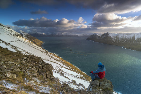 Hiker sitting on rock admiring Funningur fjord, Eysturoy island, Faroe Islands, Denmark