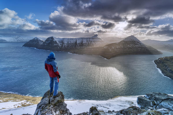 Hiker on rocks admiring the rays of sun over Funningur fjord, Eysturoy island, Faroe Islands, Denmark