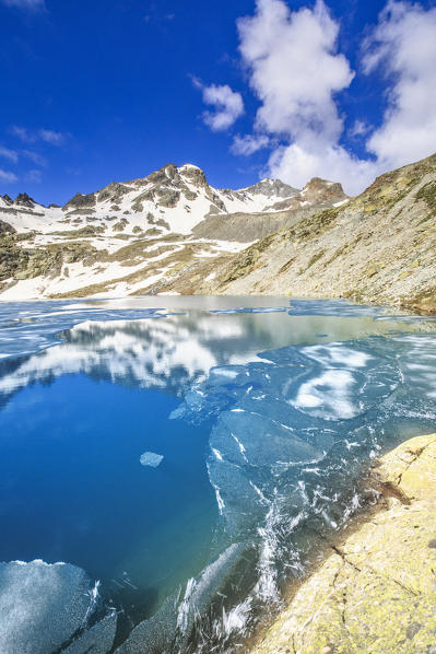 Snowy peaks mirrored in alpine lake Lej da la Tscheppa during thaw, St. Moritz, Engadin, canton of Graubunden, Switzerland