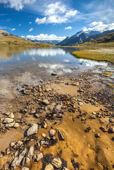 Clouds reflecting in the crystal clear water of a small Alpine lake by Gavia Pass. On the right-hand side a group of cotton-grass (eriophorus) is blooming Valfurva Valtellina,Lombardy Italy Europe