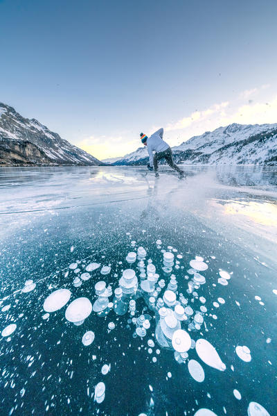 Ice hockey player skating on frozen Lake Sils covered of bubbles, canton of Graubunden, Engadine, Switzerland