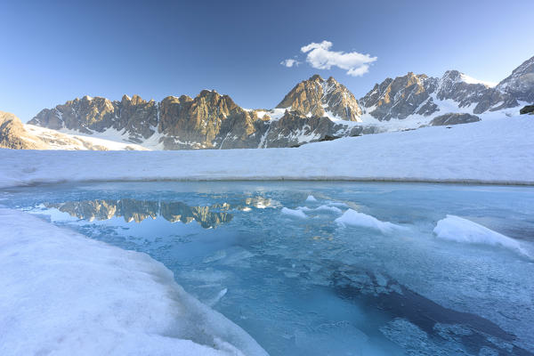 Melting ice on water surface of Forbici Lake with Bernina mountain range in background, Valmalenco, Valtellina, Lombardy, Italy