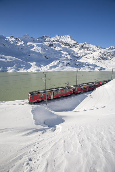 The Bernina Express train crossing Bernina Pass in winter with the snow covering the landscape at Lake Bianco, Switzerland Europe