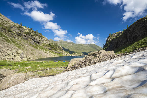 Snow on hills surrounding the hikers tents on shores of lake Zancone, Orobie Alps, Valgerola, Valtellina, Lombardy, Italy