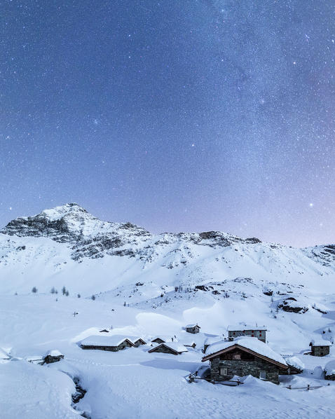 A starry night illuminates the snowy peaks and the refuge of Prabello Alp in winter. Valmalenco. Valtellina. Lombardy. Italy Europe