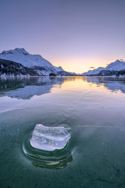 Ice block on frozen water of Lake Sils lit by a cold winter sunset, canton of Graubunden, Engadine, Switzerland