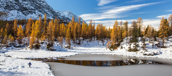 Hiker walks along the shore of the lake of Mufulè after an autumn snowfall, Valmalenco, Valtellina, Lombardy Italy Europe