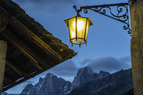 A lamp is still on, while the dawn is coming and the first lights of the day show Pizzo Badile and Pizzo Cengalo. Soglio Val Bregaglia, Canton of Graubunden, Switzerland Europe

Soglio, 
Val Bregaglia, 
Canton of Graubunden, 
Switzerland