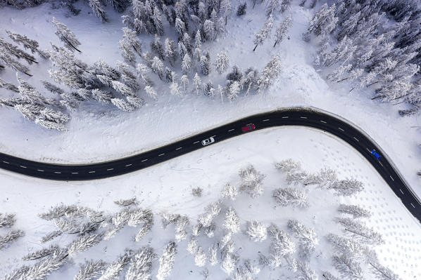 Aerial view of cars traveling on winding  mountain road crossing the snow capped woods in winter, Switzerland