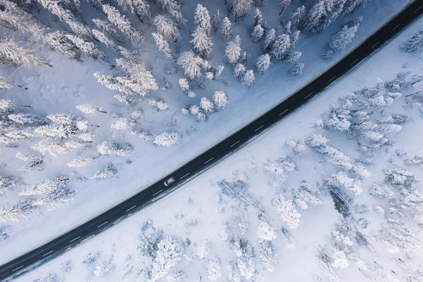 Car traveling on icy road crossing the winter forest covered with snow from above, Switzerland
