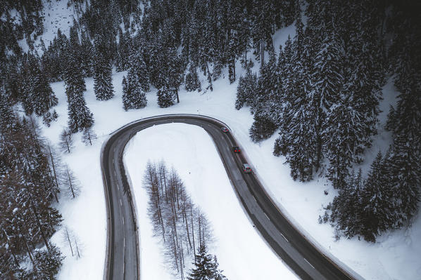 Cars driving on mountain road crossing the winter forest covered with snow