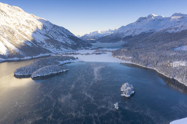 Aerial view of snowy woods and Sils Maria on shores of frozen Lake Sils, Graubunden, Engadin, Switzerland