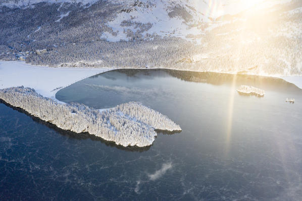 Sunbeam at dawn on frozen Lake Sils and village of Sils Maria covered with snow, Graubunden canton, Engadin, Switzerland