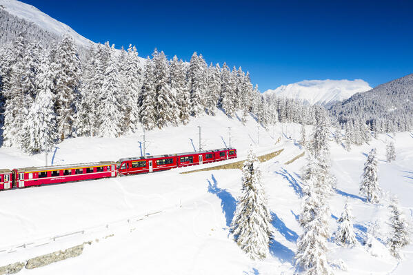 Winter sun over Bernina Express train traveling in the snowy landscape, Chapella, Graubunden canton, Engadine, Switzerland