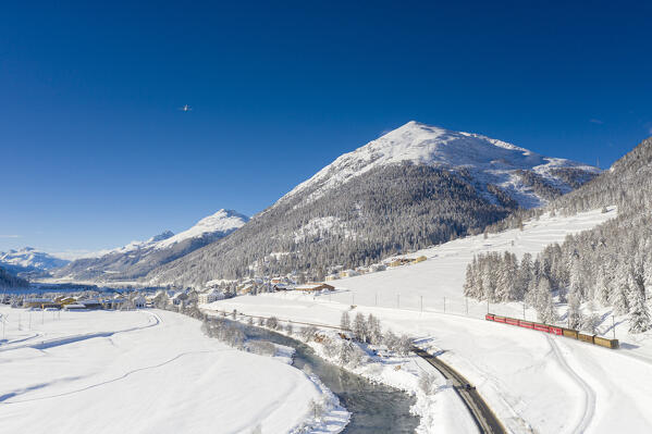 Clear sky on Bernina Express train in the snow on shore of Inn river, Madulain, Graubunden canton, Engadin, Switzerland