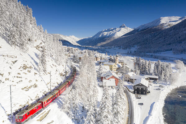 Aerial view of famous red Bernina Express train crossing the snowy village of Madulain and woods, Graubunden canton, Switzerland