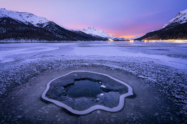 Hole in the cracked ice covering the frozen Lake Silvaplana at dawn, Maloja, Engadine, Graubunden canton, Switzerland