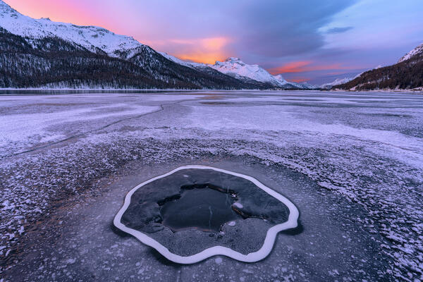 Deep hole in the cracked ice on frozen surface of Lake Silvaplana at dawn, Maloja, Engadine, Graubunden canton, Switzerland