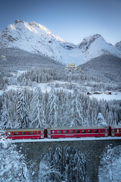 Bernina Express train on viaduct surrounding Tarasp Castle and snow capped mountains, Graubunden canton, Engadin, Switzerland