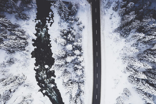 Empty road in the snow crossing the frozen forest and river from above, Engadine, Switzerland