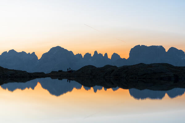 Silhouettes of hikers admiring Brenta Dolomites at dawn from Lago Nero di Cornisello, Adamello Brenta Nature Park, Trentino, Italy