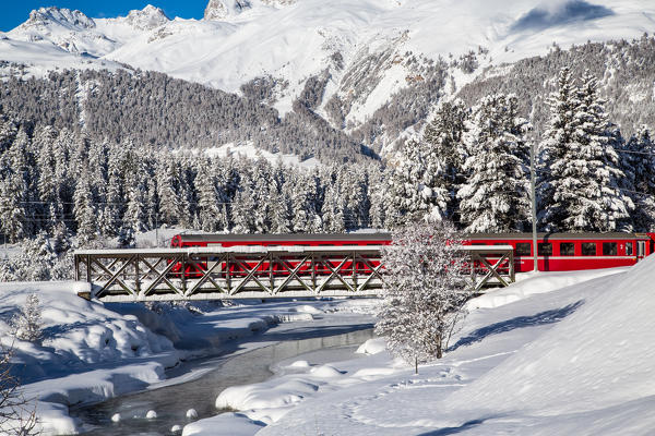 The red train of Bernina crosses a creek by a bridge. Engadine, Canton of Grisons, Switzerland Europe