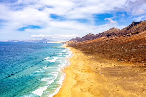 Aerial view of jeep traveling on empty Cofete Beach washed by ocean waves, Jandia, Fuerteventura, Canary Islands, Spain