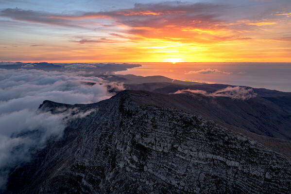 Orange sky at dawn over the ocean and Pico de la Zarza peak emerging from clouds, Jandia, Fuerteventura, Canary Islands, Spain