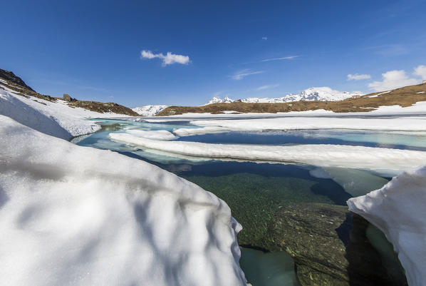 The crystal clear waters of lake Emet surrounded by snow during the thaw. Madesimo. CHiavenna Valley. Spluga Valley. Valtellina. Lombardy. Italy. Europe
