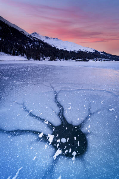 Pink sunrise over the cracked ice of the snow covered Lake Champfer, Graubunden canton, Engadine, Switzerland