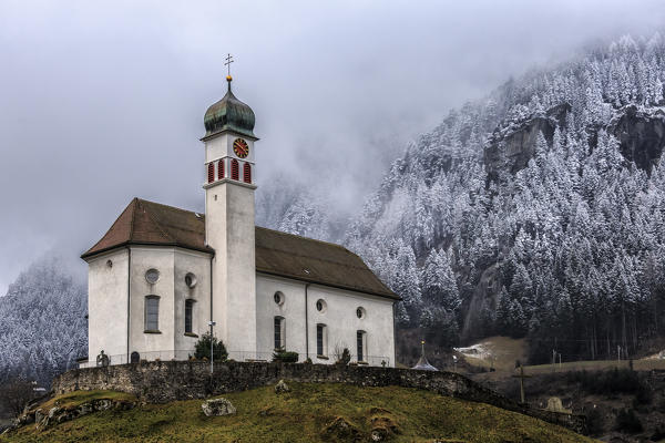 The Church of Wassen at San Gottardo after a recent snowfall that has whitened the fir trees behind it. Andermatt. Canton of Uri. Switzerland. Europe
