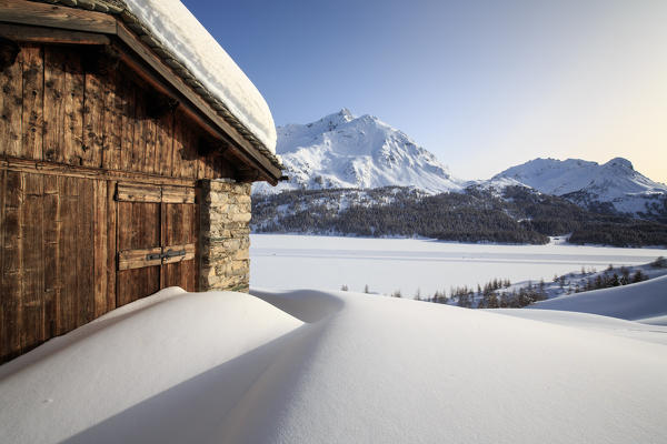 The sun covered with glazes illuminates a typical hut surrounded by snow at Maloja Pass. Engadine. Switzerland. Europe