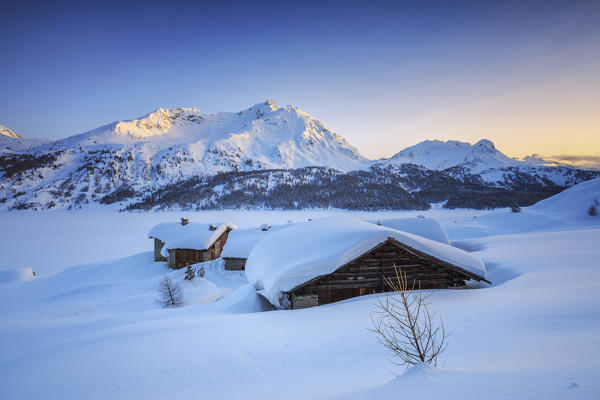 Typical alpine huts covered with snow at sunset Spluga Maloja Pass Canton of Graubunden Engadine Switzerland Europe