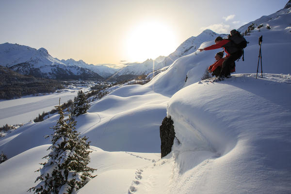 Hikers with snowshoes observe the sun set to the Maloja Pass. Engadine. Switzerland. Europe