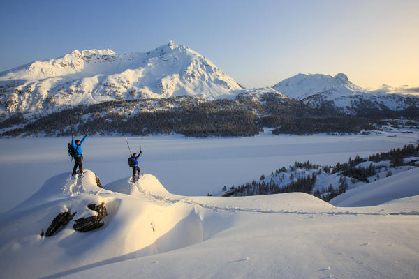 Snowshoe hikers rejoice for having reached a point with panoramic views of Lake Sils and the snow covered Piz de la Margna. Maloja Pass. Engadine. Switzerland. Europe