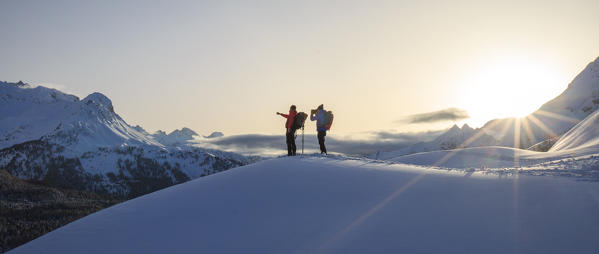 Snowshoe hikers stop to look at the snow covered peak of Piz de la Margna before the sun sets. Maloja Pass. Engadine. Switzerland. Europe