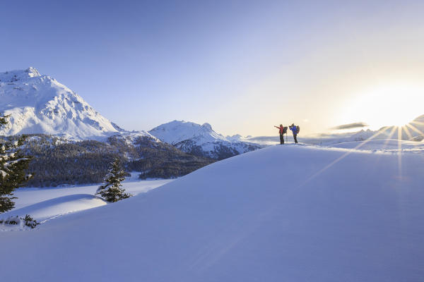 Hikers on snowshoes admire the vast panorama on the frozen lakes of the Engadine with Piz de la Margna in the background. Canton of Graubunden. Maloja Pass. Engadine. Switzerland. Europe